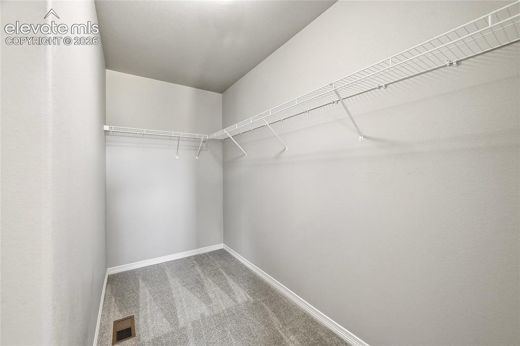 Image 18 of 30: Walk-in closet featuring wire shelving, gray textured walls, and gray carpe
