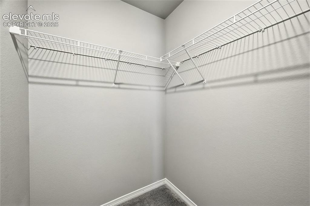 Image 20 of 30: Walk-in closet featuring white wire shelving, white walls, and gray carpeti