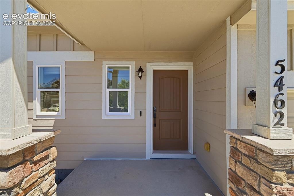 Image 5 of 30: Covered entryway featuring a paneled wood-finish door, sconce lighting, and