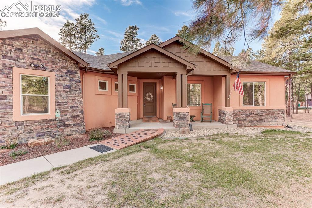 Caption: Craftsman-style house featuring stone siding, covered porch, a front lawn, and stucco siding