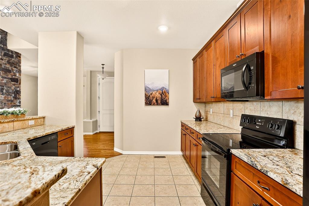 Image 16 of 45: Kitchen with black appliances, light stone counters, backsplash, solid wood