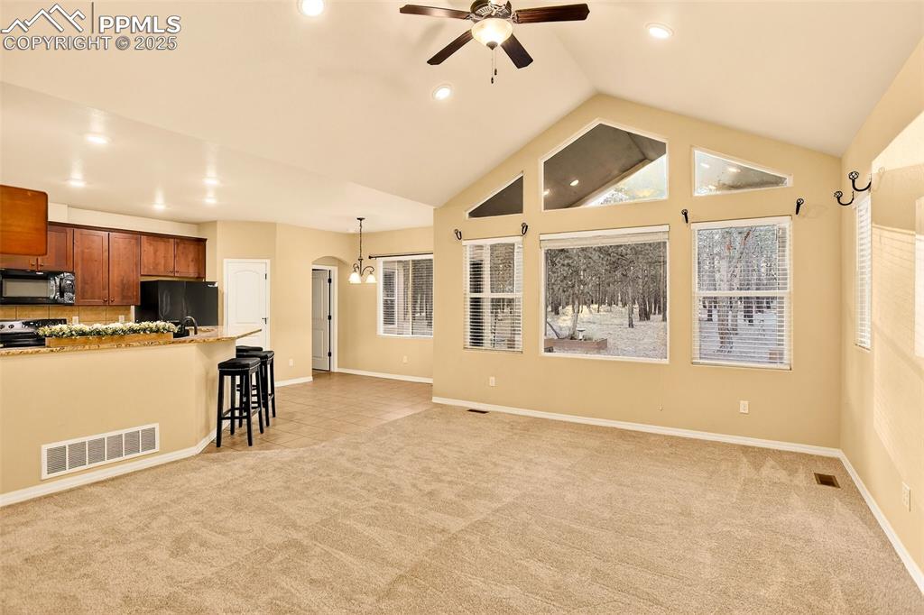 Image 20 of 45: Living area with arched walkways, new carpet, a ceiling fan, high vaulted c