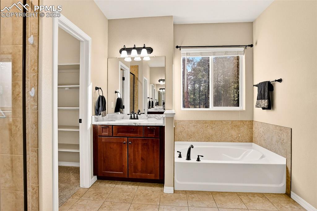 Image 37 of 45: Bathroom with a bath, vanity, light tile patterned floors, and a walk in cl