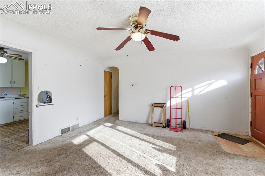 Image 6 of 35: Unfurnished living room featuring a ceiling fan, carpet floors, arched walk