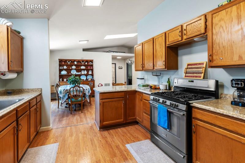 Image 15 of 29: Kitchen featuring gas range, brown cabinetry, lofted ceiling, light wood-st