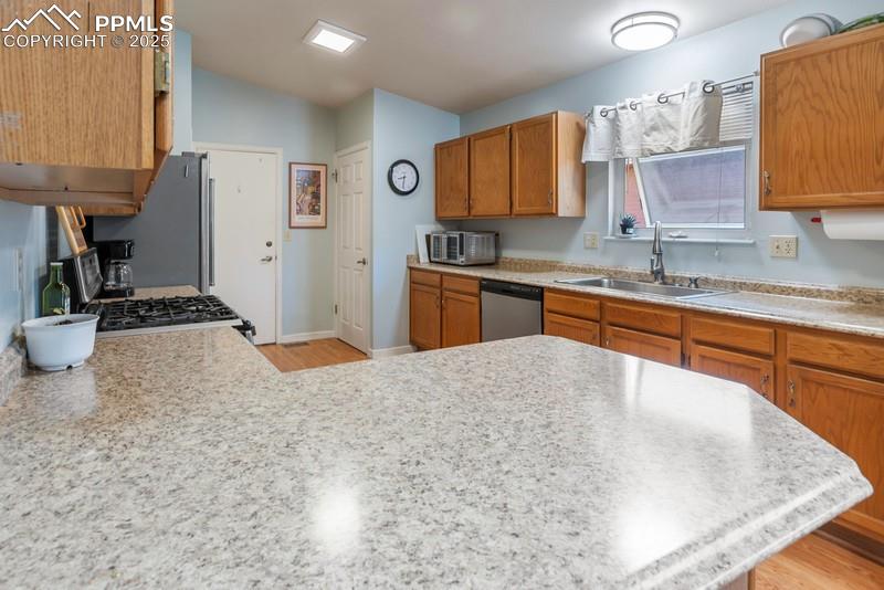 Image 17 of 29: Kitchen with brown cabinets, light wood-style floors, stainless steel appli