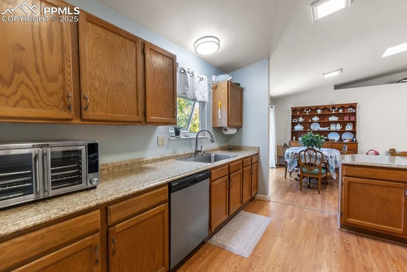 Image 19 of 29: Kitchen with brown cabinets, light wood-style flooring, stainless steel dis