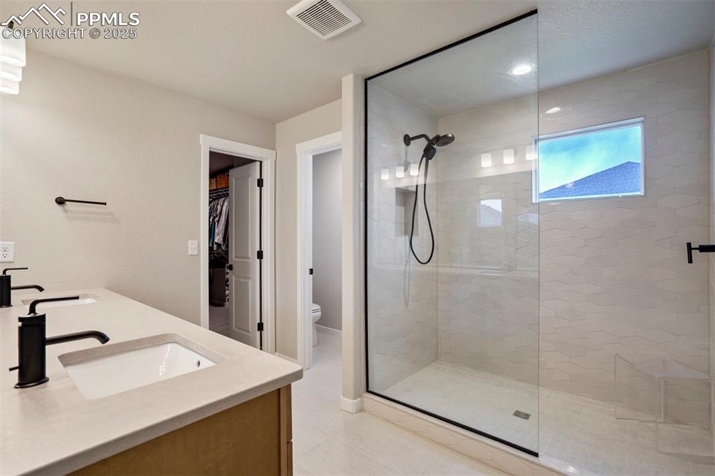 Image 17 of 47: Bathroom featuring a shower stall, toilet, double vanity, a walk in closet,