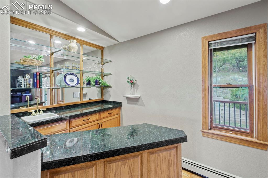 Image 18 of 50: Indoor wet bar featuring a textured wall, a baseboard radiator, tile counte