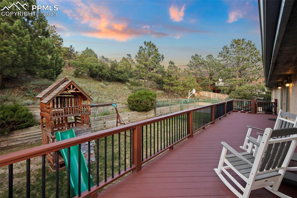 Image 44 of 50: Deck with a playground, a fenced backyard, and view of wooded area