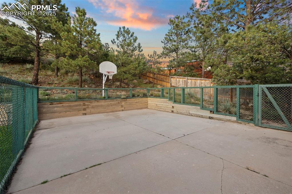 Image 45 of 50: View of sport court with a fenced backyard, basketball hoop, and a patio ar