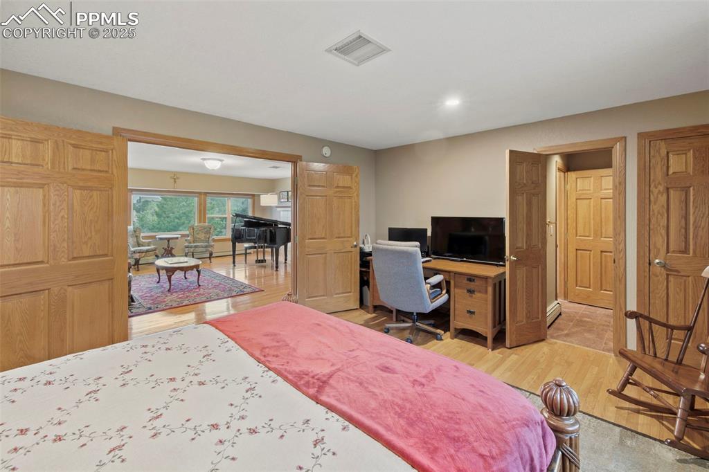Image 8 of 50: Bedroom with light wood finished floors, a desk, recessed lighting, and a b