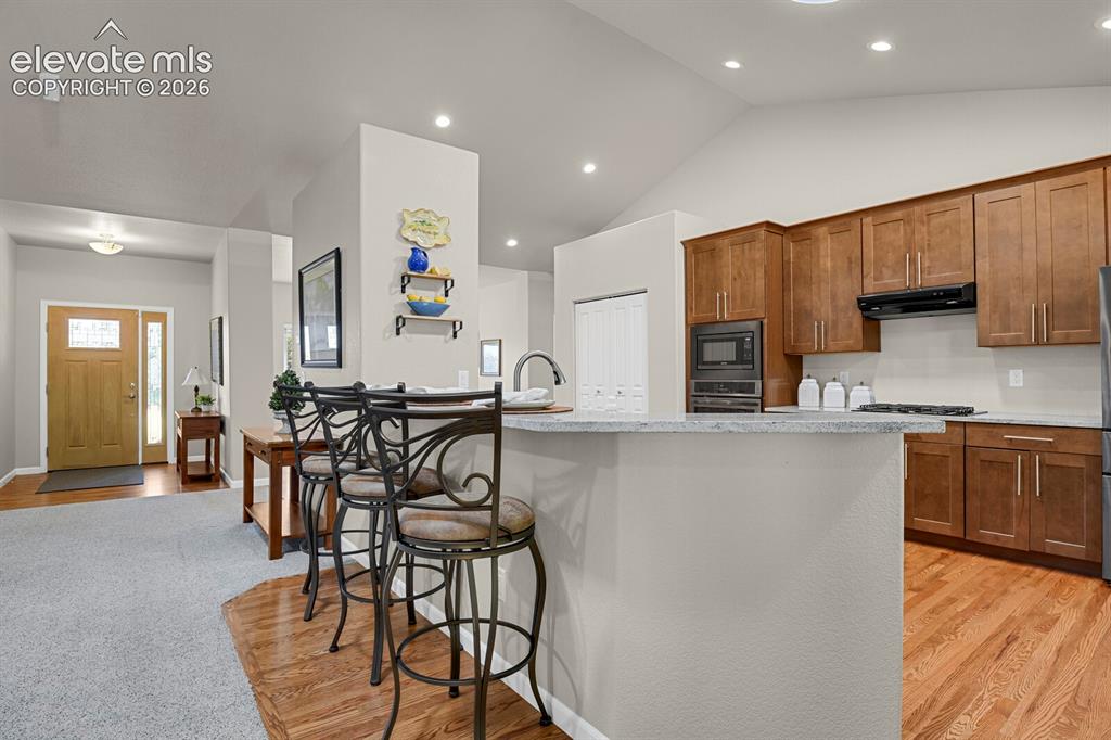 Image 12 of 46: Kitchen featuring wood cabinetry, stone-surface breakfast bar, built-in wal