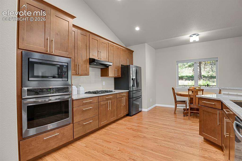Image 16 of 46: Kitchen featuring wood-finish cabinetry, stone-surface countertops, vaulted