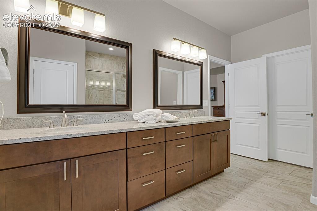 Image 23 of 46: Double vanity featuring wood cabinetry, stone countertops, dual under-mount