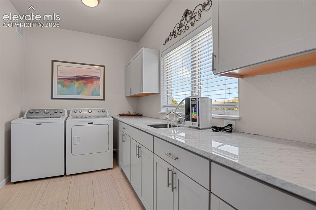 Image 32 of 46: Laundry room featuring shaker-style cabinetry, stone-finish countertops, ti
