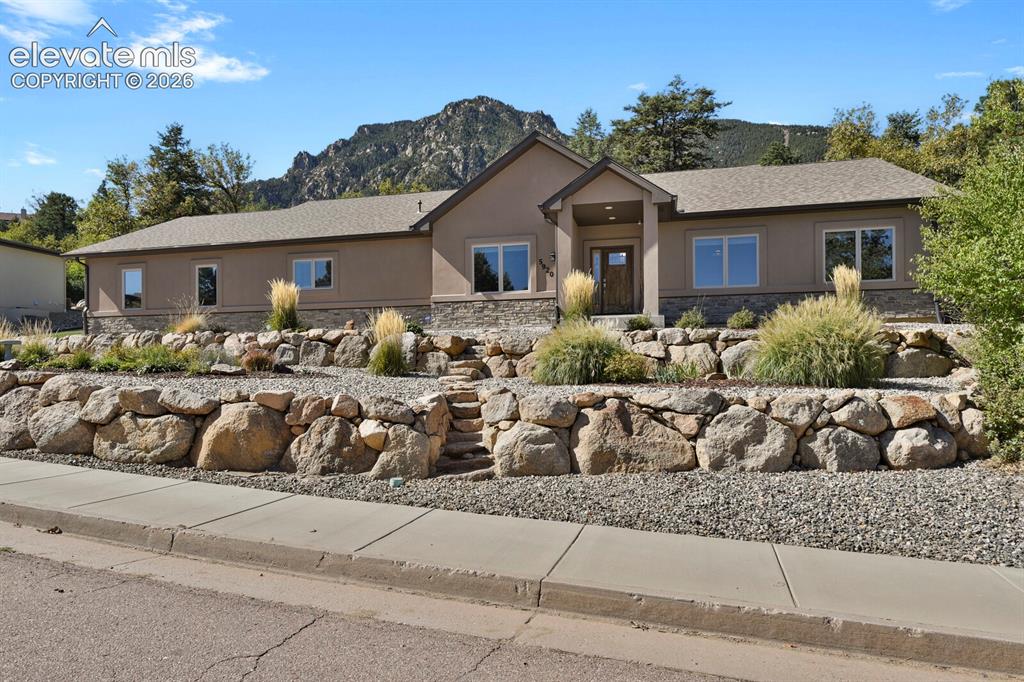 Image 37 of 46: Stucco and stone exterior featuring tiered boulder retaining walls, integra