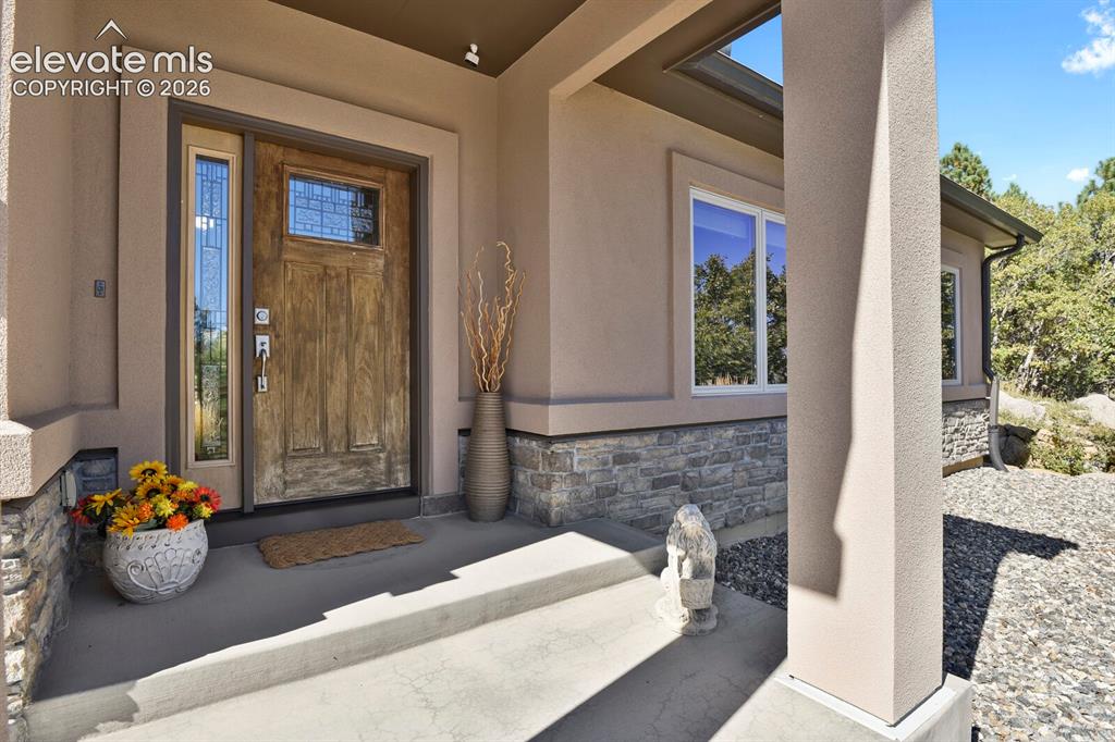 Image 5 of 46: Covered entryway featuring a wood-finish front door with glass inlay, stone