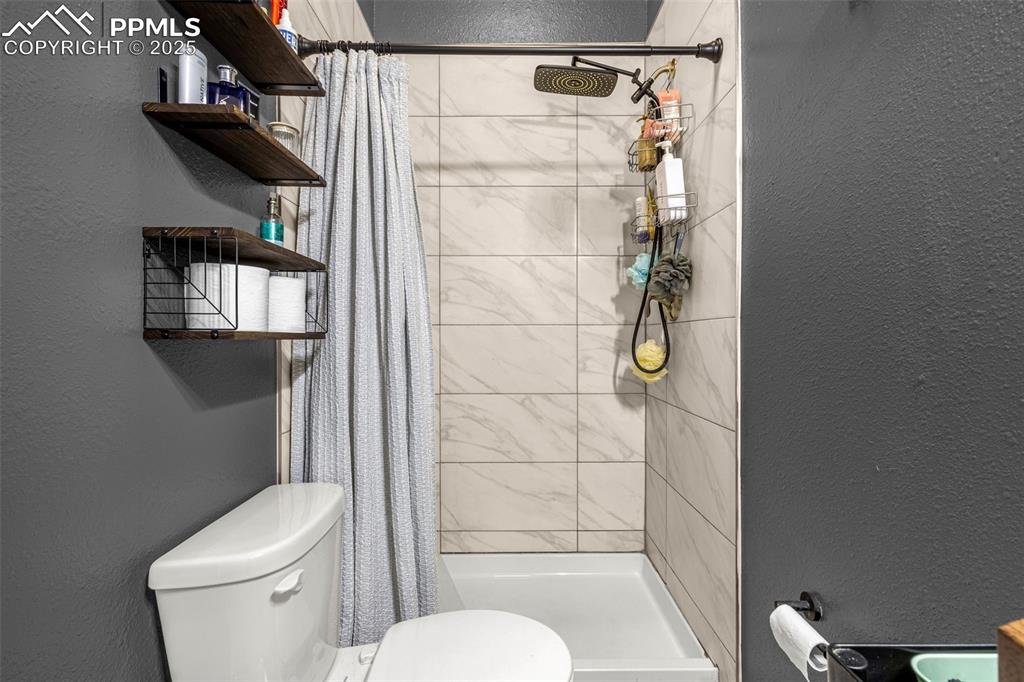 Image 16 of 36: Full bathroom with a textured wall, toilet, and a shower stall