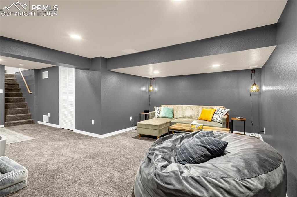 Image 23 of 36: Carpeted living area with a textured wall, baseboards, stairs, and recessed