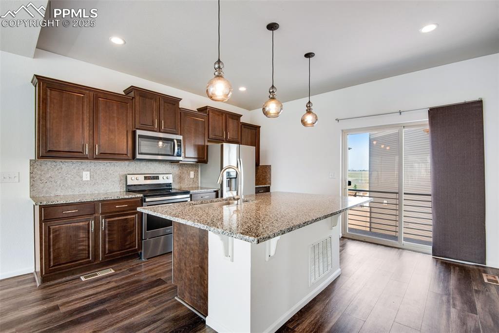 Image 10 of 39: Kitchen with tasteful backsplash, stainless steel appliances, light stone c