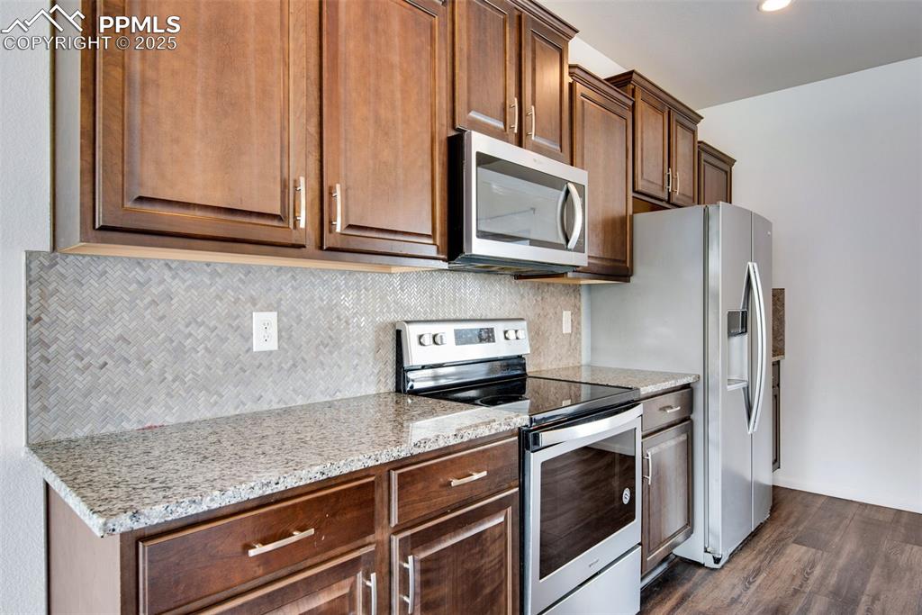 Image 11 of 39: Kitchen with stainless steel appliances, backsplash, light stone counters,