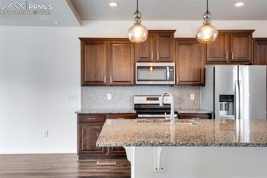 Image 12 of 39: Kitchen with tasteful backsplash, stainless steel appliances, light stone c