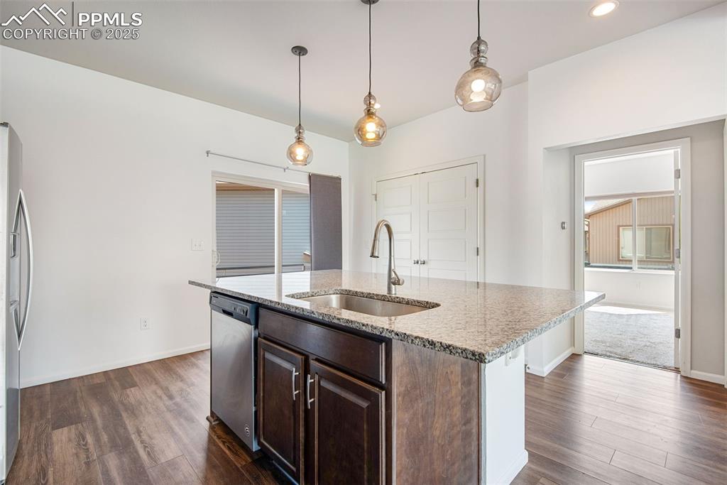 Image 14 of 39: Kitchen featuring dark brown cabinetry, light stone counters, decorative li