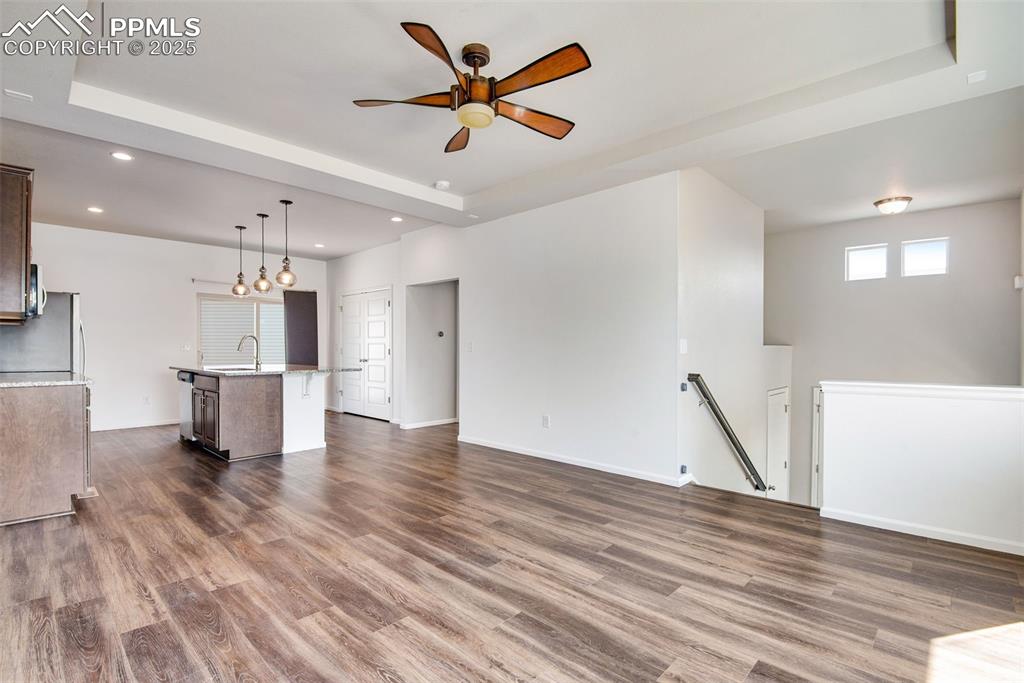 Image 8 of 39: Unfurnished living room featuring a raised ceiling, a ceiling fan, dark woo
