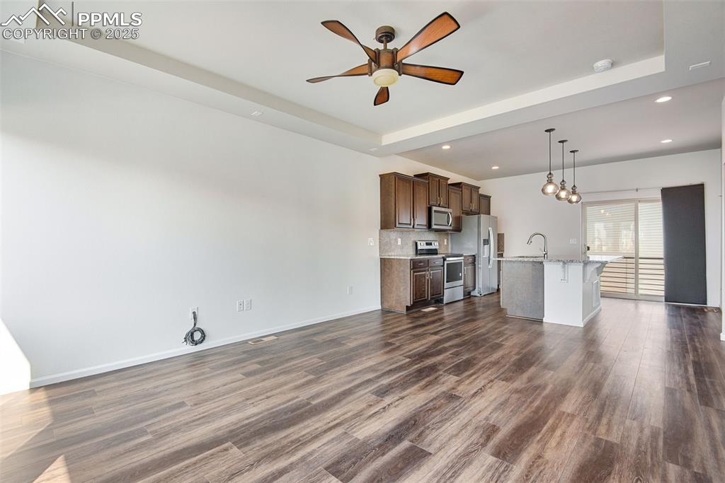 Image 9 of 39: Unfurnished living room with a raised ceiling, ceiling fan, dark wood-style