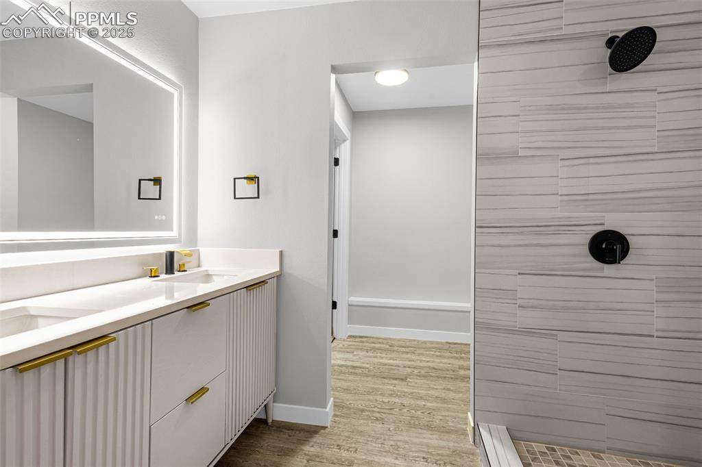 Image 10 of 37: Full bath featuring a tile shower, double vanity, and wood finished floors