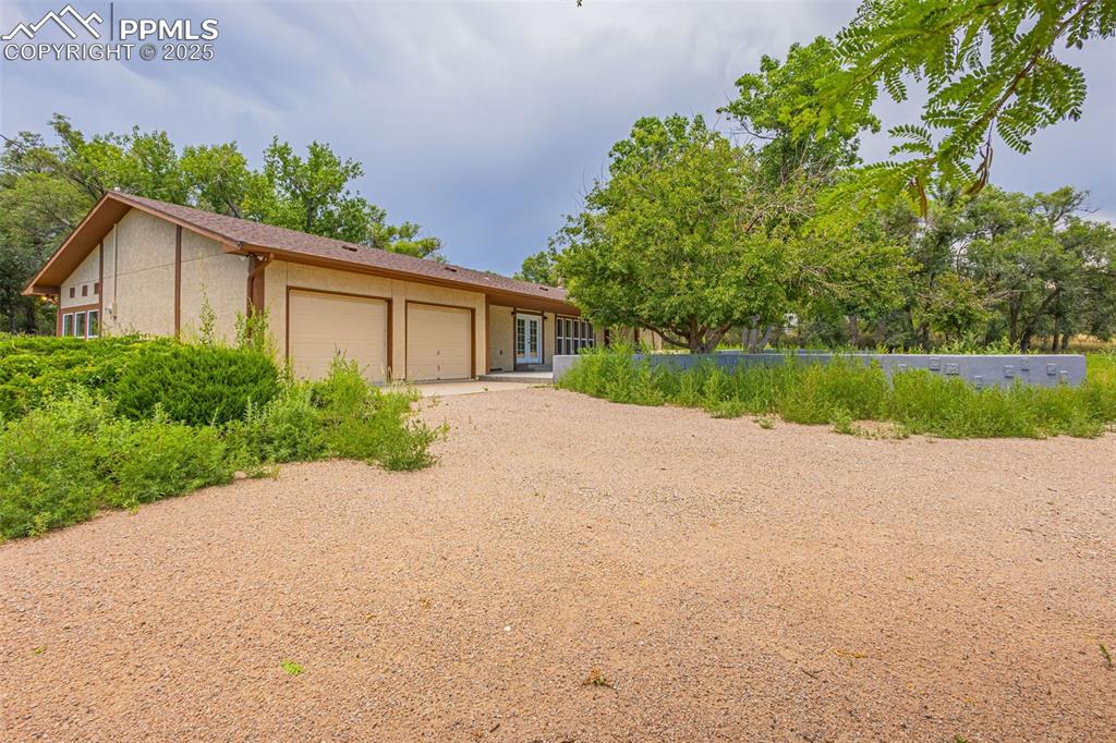 Image 24 of 37: Single story home with a garage, gravel driveway, and stucco siding