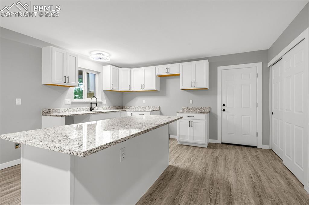 Image 5 of 37: Kitchen with light wood-style flooring, white cabinetry, light stone counte