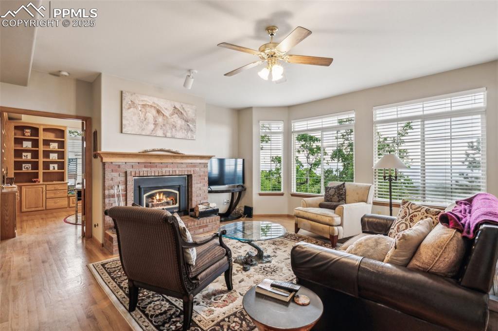 Image 15 of 43: Living room featuring a brick fireplace, a ceiling fan, and wood floors