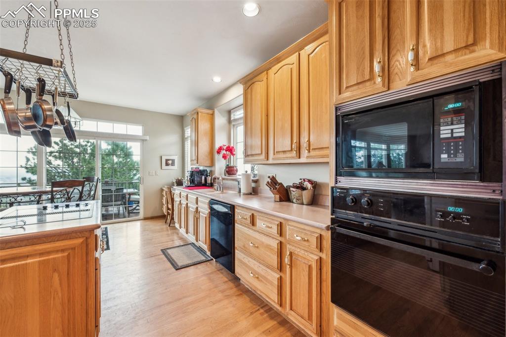 Image 9 of 43: Kitchen with black appliances, light wood flooring, light countertops, rece