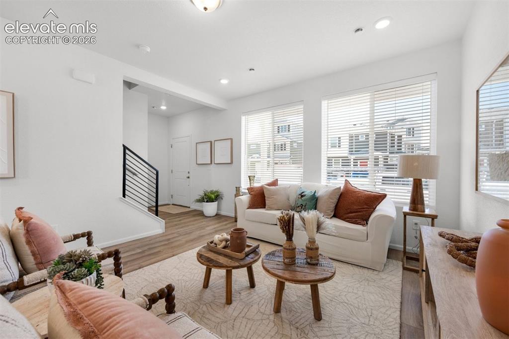 Image 7 of 35: Bright living area featuring wood-finish flooring, multiple windows with bl