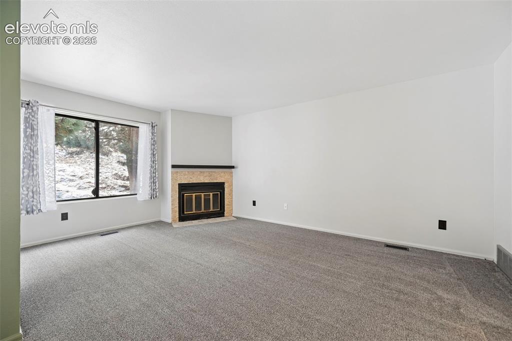 Image 10 of 25: Recessed fireplace with a stone surround, large window, and gray carpeting