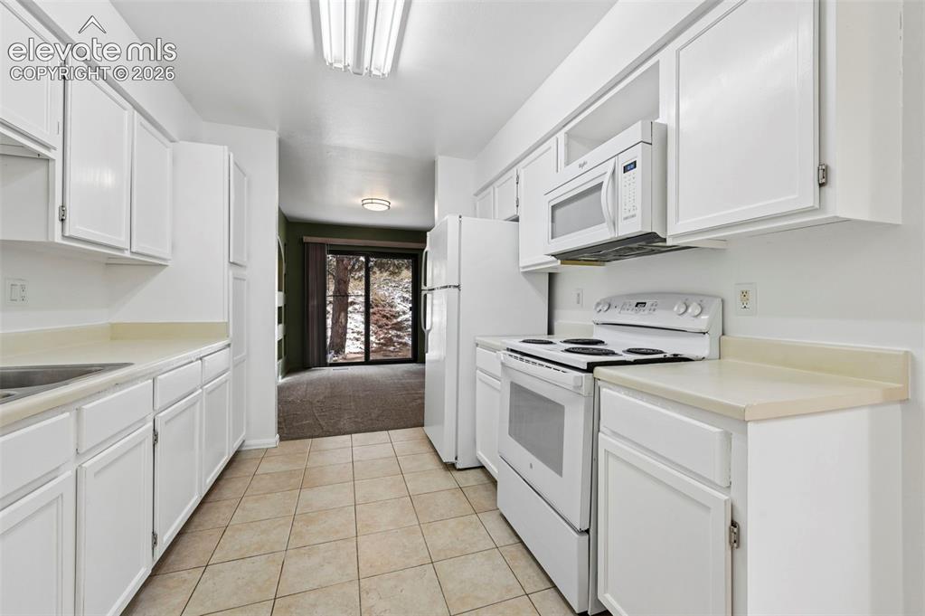 Image 5 of 25: Galley kitchen featuring white cabinetry, tile flooring, stainless steel ap