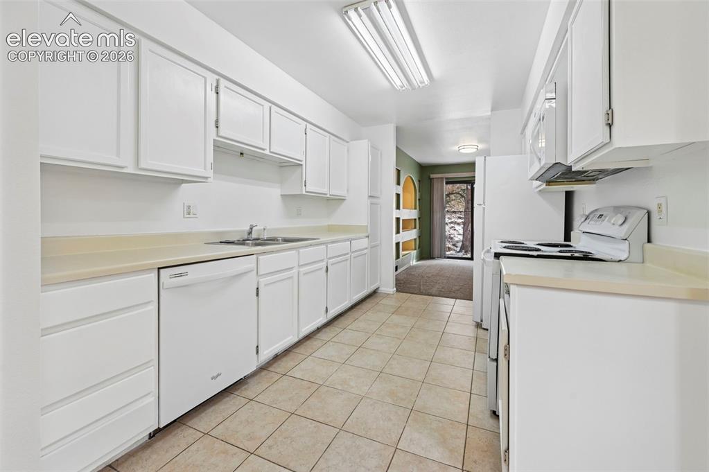 Image 6 of 25: Galley kitchen featuring white cabinetry, light-toned countertops, a stainl