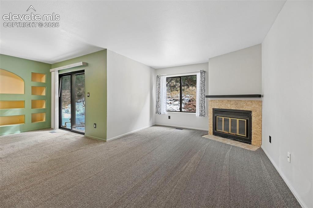Image 8 of 25: Carpeted room featuring a stone-clad fireplace with metal insert, built-in 