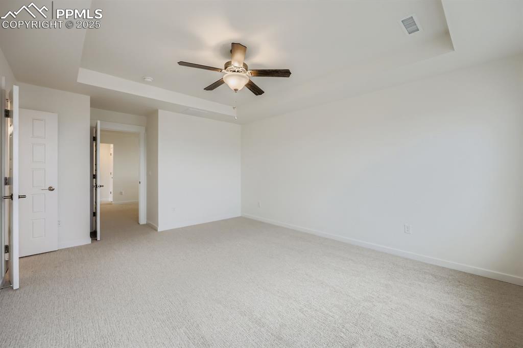 Image 15 of 28: Unfurnished bedroom with a tray ceiling, ceiling fan, and light colored car