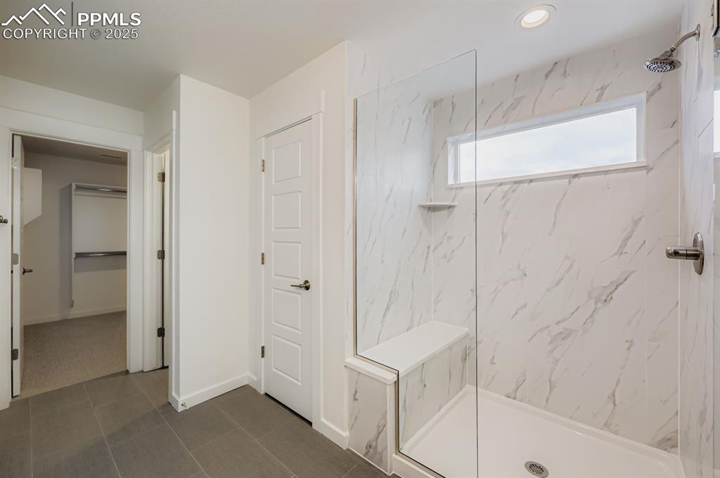 Image 17 of 28: Full bathroom featuring a marble finish shower, a closet, and dark tile pat
