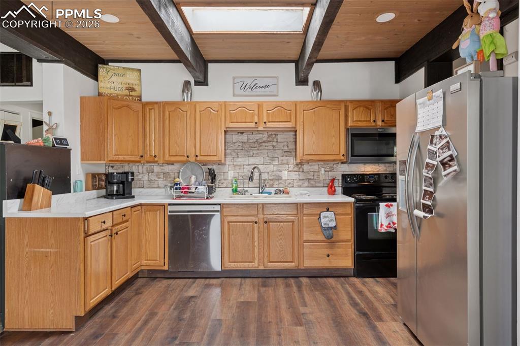 Image 12 of 49: Kitchen featuring wood cabinetry, stone-like tile backsplash, stainless ste