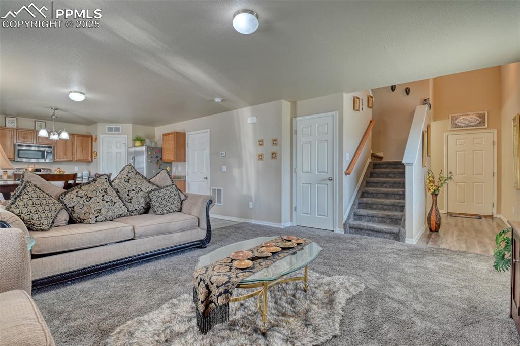 Image 13 of 43: Living area with carpet flooring, a chandelier, and stairway