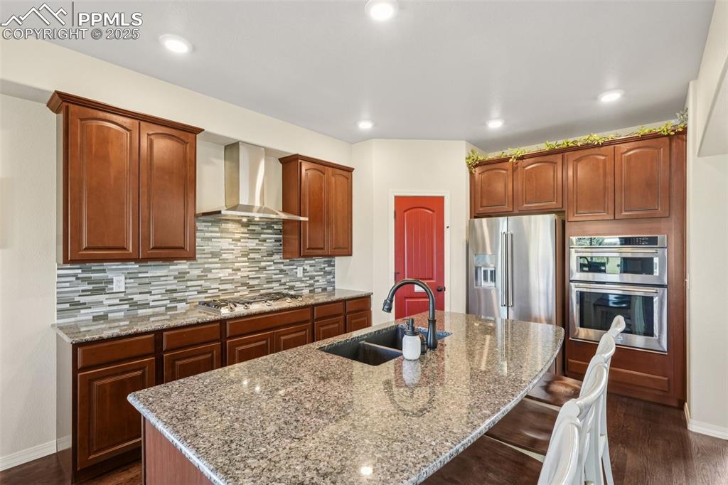 Image 12 of 46: Kitchen with stainless steel appliances, wall chimney range hood, an island