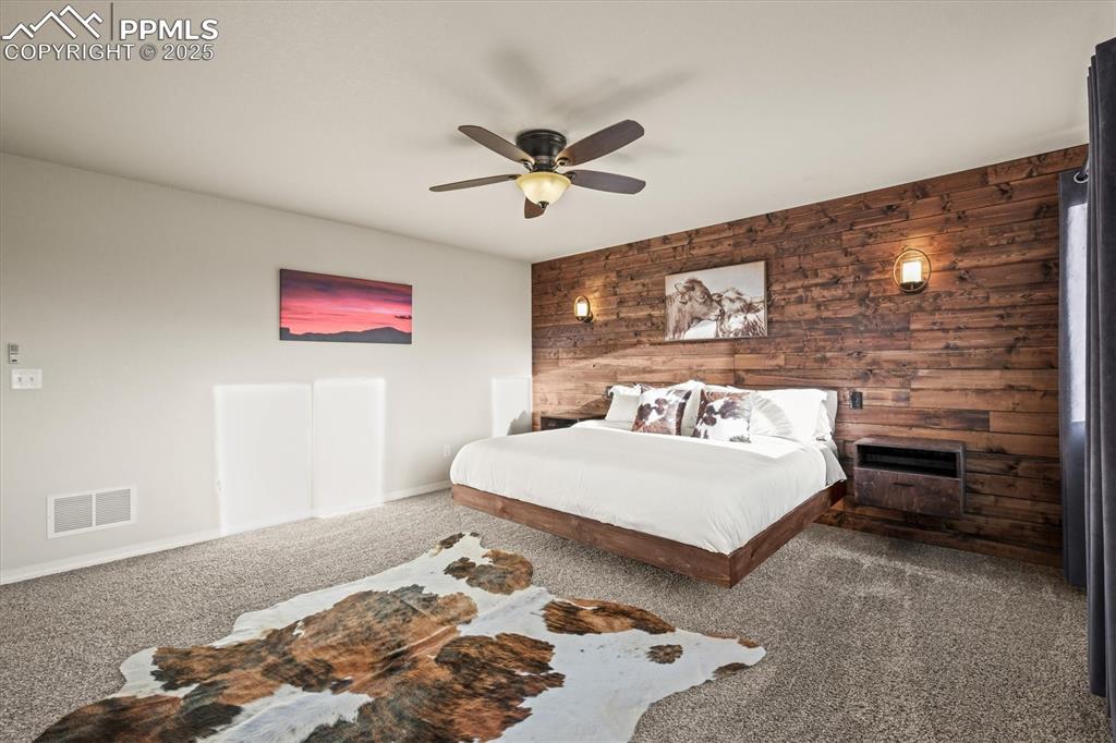 Image 22 of 46: Carpeted bedroom featuring ceiling fan, wood walls, visible vents, and base