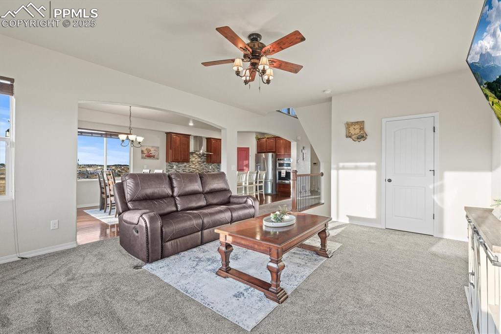 Image 4 of 46: Living room featuring ceiling fan with notable chandelier, arched walkways,