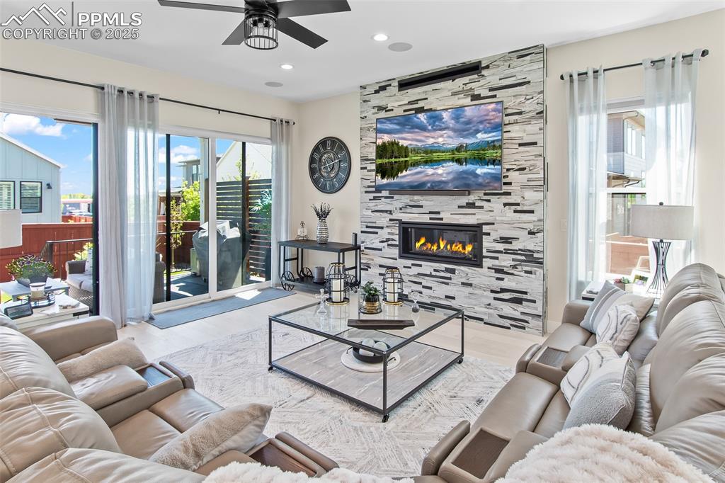 Image 12 of 48: Living room with wood finished floors, a tile fireplace, a ceiling fan, and