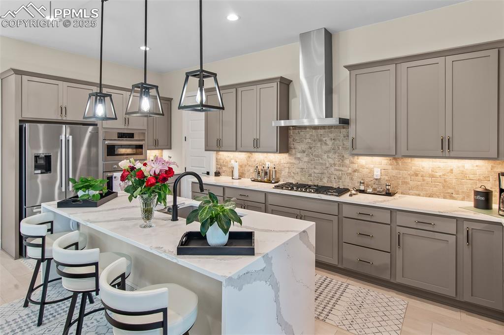 Image 17 of 48: Kitchen with gray cabinetry, light stone counters, pendant lighting, backsp