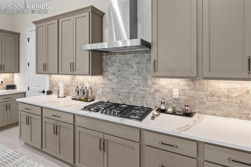 Image 18 of 48: Kitchen featuring backsplash, gray cabinets, light stone countertops, wall